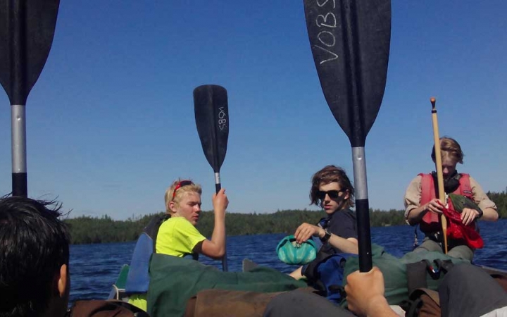 Students sitting in canoes raise their paddles into the air.